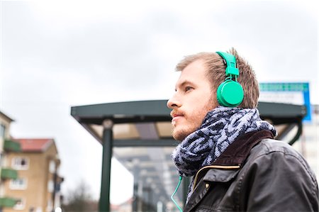 Side view of man listening music at bus stop against clear sky Photographie de stock - Premium Libres de Droits, Code: 6127-08689015