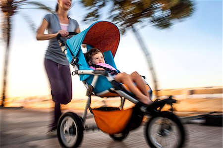 Woman jogging while pushing her daughter in a stroller. Stock Photo - Premium Royalty-Free, Code: 6128-08747481