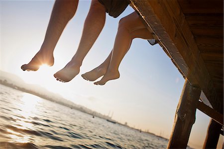 simsearch:6115-06732976,k - Two pairs of legs dangling off a wooden pier. Fotografie stock - Premium Royalty-Free, Codice: 6128-08747495