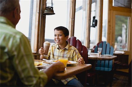 Boy with cream around his face grinning while sitting in a diner with his father. Stock Photo - Premium Royalty-Free, Code: 6128-08747565
