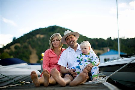 Portrait of a smiling mid-adult couple sitting with their young son on a wooden jetty. Photographie de stock - Premium Libres de Droits, Code: 6128-08747534