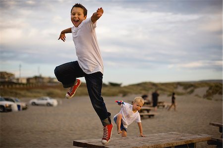 simsearch:6128-08767321,k - Two boys jumping from picnic tables at the beach. Foto de stock - Royalty Free Premium, Número: 6128-08747693