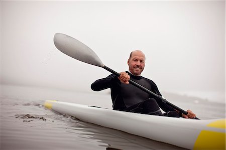 Male kayaker smiles for a portrait as he paddles in the waters of a foggy harbour. Stockbilder - Premium RF Lizenzfrei, Bildnummer: 6128-08747707