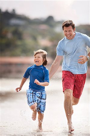 simsearch:400-04114591,k - Young boy laughs as he runs away from his smiling father as they play on a beach and pose for a portrait. Stock Photo - Premium Royalty-Free, Code: 6128-08747807