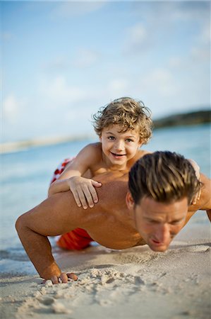 strong depth of field - Portrait of a young boy lying on his fathers back as he does press ups on a sandy beach. Stock Photo - Premium Royalty-Free, Code: 6128-08747946