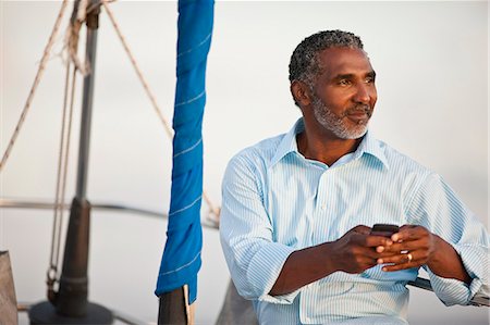 Mature man looking out at view of water from boat, holding cell phone. Stock Photo - Premium Royalty-Free, Code: 6128-08748041