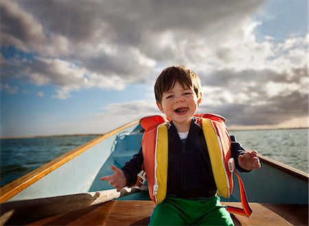 Portrait of toddler boy sitting in row boat with lifevest on, sticking out tongue. Stock Photo - Premium Royalty-Free, Code: 6128-08748197