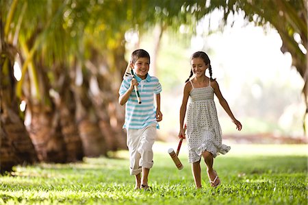 Brother and sister running together holding croquet mallets. Stock Photo - Premium Royalty-Free, Code: 6128-08766560