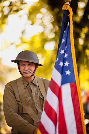 Mature male reenactor wearing an American World War steel combat helmet and uniform and holding up American flag poses for a portrait. Stockbilder - Premium RF Lizenzfrei, Bildnummer: 6128-08766662