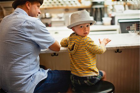 Young boy looks over his shoulder as he sits with his father at a restaurant counter. Foto de stock - Sin royalties Premium, Código: 6128-08766634