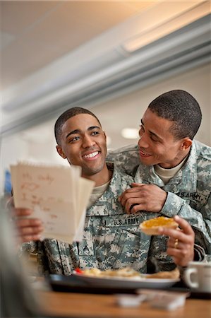 Young soldier looks over his friend's shoulder as he reads a  letter during breakfast. Photographie de stock - Premium Libres de Droits, Code: 6128-08766713