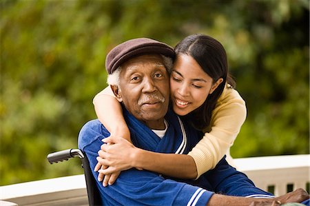 Young woman leans over and embraces her grandfather sitting in a wheelchair as they pose for a portrait on a porch. Stock Photo - Premium Royalty-Free, Code: 6128-08766971