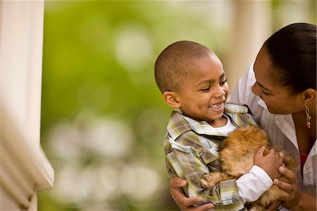 shoulders mom - Young boy smiles as he holds a puppy and sits with his mother on a porch. Photographie de stock - Premium Libres de Droits, Code: 6128-08766972