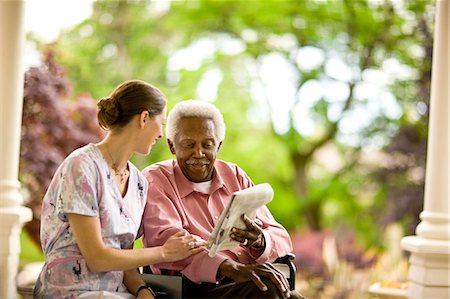 simsearch:841-07201661,k - Female nurse laughs and talks with a senior man as they sit on a porch and look at a newspaper. Stock Photo - Premium Royalty-Free, Code: 6128-08766975