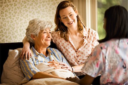 patient happy in bed - Young woman sits on the edge of a bed and puts a reassuring arm around a senior woman. Stock Photo - Premium Royalty-Free, Code: 6128-08766985