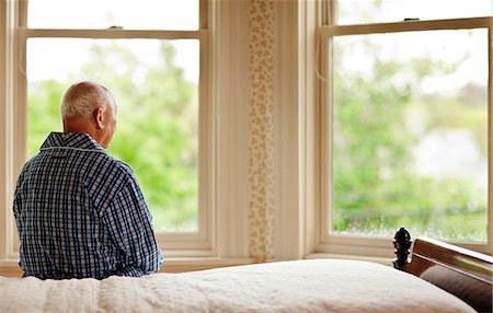 rear of house - Senior man looking out his bedroom window while sitting on a bed in his pajamas. Foto de stock - Sin royalties Premium, Código: 6128-08767043