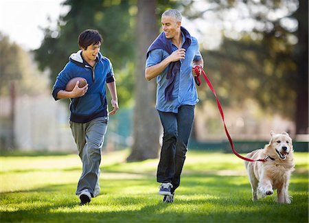 simsearch:6128-08738251,k - Smiling mid adult man and his son having fun jogging together in the park with their dog. Foto de stock - Sin royalties Premium, Código: 6128-08767151