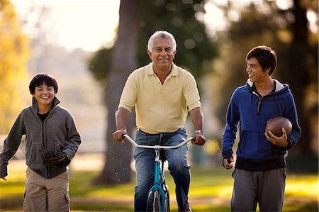simsearch:6109-08537037,k - Smiling senior man having fun riding a bicycle while in a park with his two grandsons. Stock Photo - Premium Royalty-Free, Code: 6128-08767231