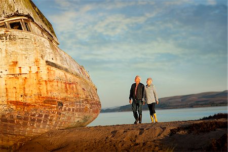 Senior couple walking on the beach hand-in-hand next to an obsolete boat. Stock Photo - Premium Royalty-Free, Code: 6128-08767333