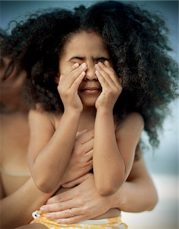 family portraits in frames - Young girl with curly black hair rubbing her eyes while being hugged by a woman from behind. Photographie de stock - Premium Libres de Droits, Code: 6128-08780351