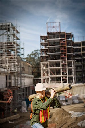 Mid-adult construction worker carrying a large pipe on his shoulder at an outdoor construction site. Stock Photo - Premium Royalty-Free, Code: 6128-08780394