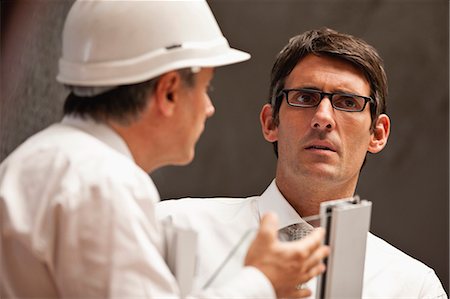 Businessman wearing eyeglasses looks concerned as a a male colleague in a hardhat talks to him. Stock Photo - Premium Royalty-Free, Code: 6128-08780643