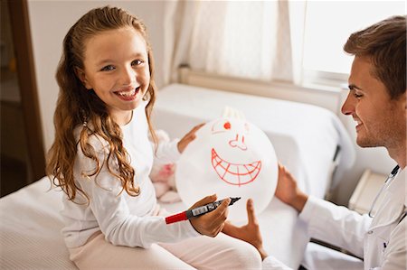 Male doctor sitting with his young female patient, drawing face on balloon made from rubber glove. Stock Photo - Premium Royalty-Free, Code: 6128-08780790