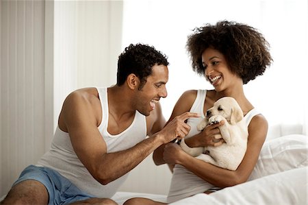Couple plays with puppies on a bed. Fotografie stock - Premium Royalty-Free, Codice: 6128-08780863