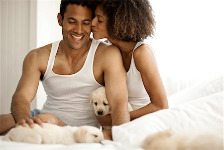 romantic boy hug images - Woman holds a puppy and kisses her boyfriends cheek. Photographie de stock - Premium Libres de Droits, Code: 6128-08780862