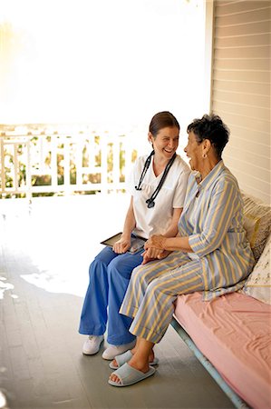 Elderly patient sitting on the deck of rest-home with her nurse and laughing. Photographie de stock - Premium Libres de Droits, Code: 6128-08780940