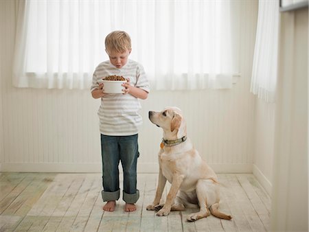 dog owner (male) - Young boy holding bowl of dog food as his dog looks up at it. Stock Photo - Premium Royalty-Free, Code: 6128-08780908