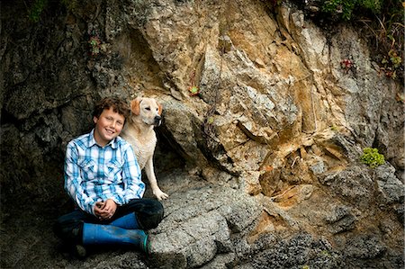 simsearch:649-09207273,k - Boy sitting with his dog on rocks at the beach. Fotografie stock - Premium Royalty-Free, Codice: 6128-08780916