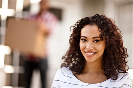 simsearch:6128-08738561,k - Portrait of smiling mid-adult woman with her boyfriend in the background. Stock Photo - Premium Royalty-Free, Code: 6128-08781053
