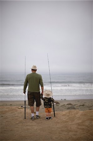 Young boy and his father walking along a beach carrying fishing rods and wearing hats. Stock Photo - Premium Royalty-Free, Code: 6128-08798745