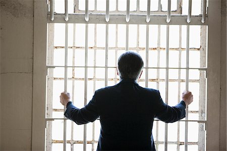 simsearch:695-03379065,k - Businessman standing in front of a barred window in a derelict building. Foto de stock - Royalty Free Premium, Número: 6128-08798724