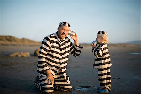 Mid-adult father and his son playing with a tin can phone on a beach while wearing striped prisoner costumes. Photographie de stock - Premium Libres de Droits, Code: 6128-08798730