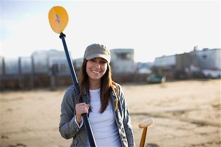 Portrait of a smiling mid-adult woman holding an oar on a sandy beach. Stock Photo - Premium Royalty-Free, Code: 6128-08798736