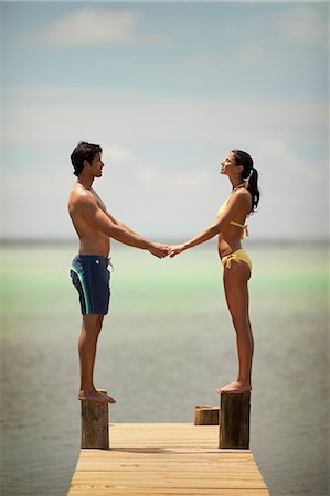simsearch:6108-08662338,k - Young couple hold hands face to face while balancing on an ocean pier. Photographie de stock - Premium Libres de Droits, Code: 6128-08798804