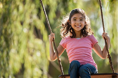 simsearch:6128-08748026,k - Smiling young girl swings on a rope swing in a garden. Photographie de stock - Premium Libres de Droits, Code: 6128-08798979