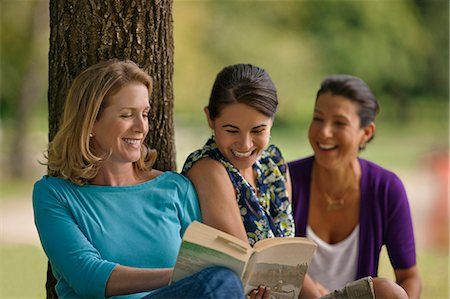 simsearch:6102-08388034,k - Happy friends reading a book together under a tree at the park. Fotografie stock - Premium Royalty-Free, Codice: 6128-08799021