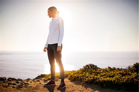 simsearch:6128-08727475,k - Young woman takes a break from her sunrise jog along the cliffs to admire the view of the ocean. Photographie de stock - Premium Libres de Droits, Code: 6128-08727469