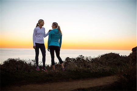 simsearch:6128-08727475,k - Smiling young woman gently encourages her friend to continue their sunrise jog along the cliffs. Photographie de stock - Premium Libres de Droits, Code: 6128-08727470