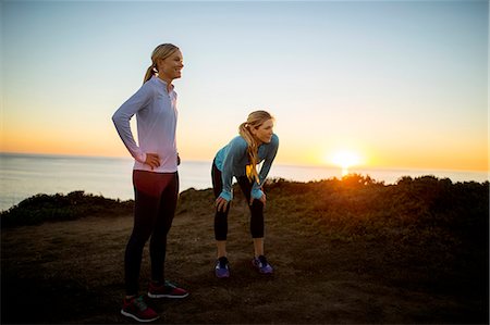 simsearch:6128-08727475,k - Two smiling young women take a break from their sunrise jog along the cliffs to admire the view of the ocean. Photographie de stock - Premium Libres de Droits, Code: 6128-08727472