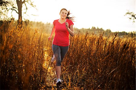 simsearch:6128-08727475,k - Young woman goes for a countryside run through tall grasses in the late afternoon sunlight. Photographie de stock - Premium Libres de Droits, Code: 6128-08727479