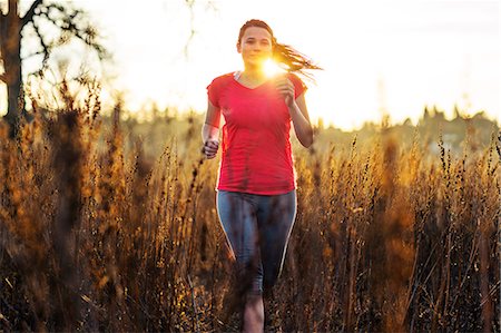 simsearch:6128-08727475,k - Young woman goes for a countryside run through tall grasses in the late afternoon sunlight. Photographie de stock - Premium Libres de Droits, Code: 6128-08727484
