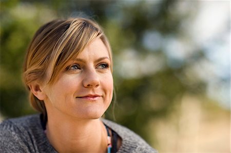 simsearch:6128-08727668,k - Smiling young woman looks thoughtfully into the distance as she sits outside. Stock Photo - Premium Royalty-Free, Code: 6128-08727548