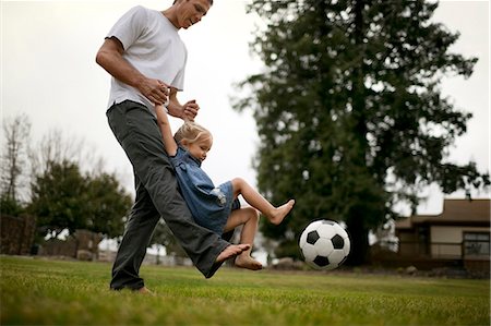 simsearch:6128-08747735,k - Smiling father teaches his little girl how to kick a soccer ball on the lawn. Stockbilder - Premium RF Lizenzfrei, Bildnummer: 6128-08727501