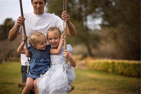 simsearch:6128-08767314,k - Two smiling little girls have fun being pushed on a tree swing by their father. Stock Photo - Premium Royalty-Free, Code: 6128-08727511