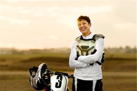 safety helmet dirt - Portrait of a smiling young female motocross rider standing in front of her bike at the track. Photographie de stock - Premium Libres de Droits, Code: 6128-08727538