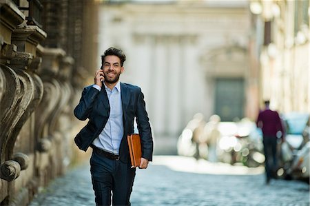 Cheerful young businessman makes a call as he is running along the street late for work. Stock Photo - Premium Royalty-Free, Code: 6128-08727676